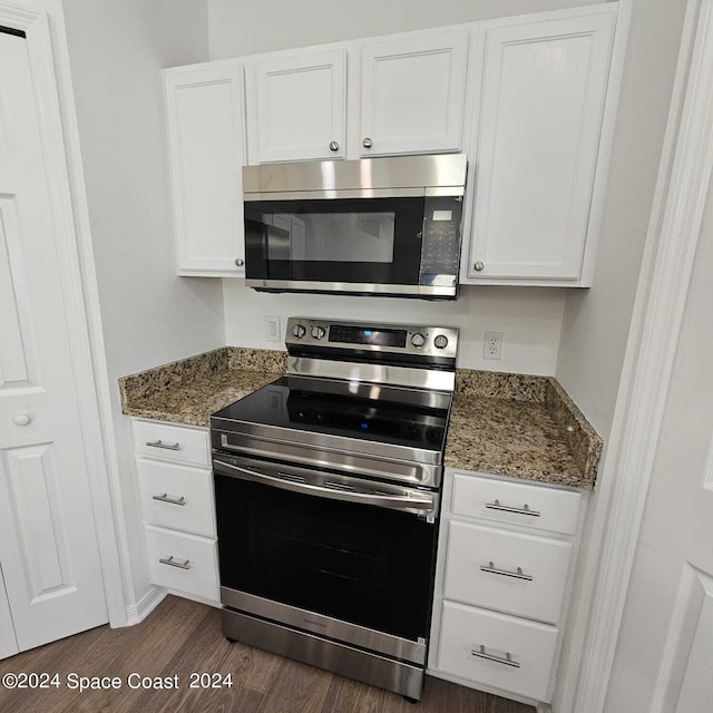 kitchen featuring appliances with stainless steel finishes, dark wood-type flooring, dark stone counters, and white cabinetry