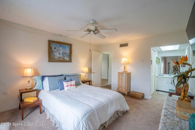 carpeted bedroom with a skylight, ceiling fan, connected bathroom, and a textured ceiling