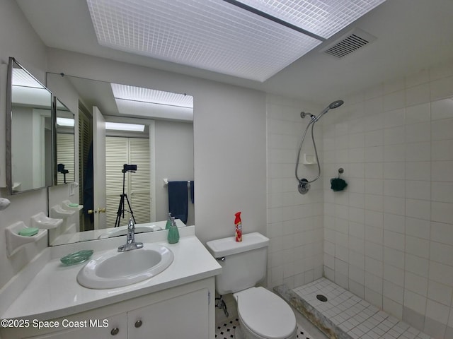 full bathroom featuring a tile shower, vanity, visible vents, and toilet