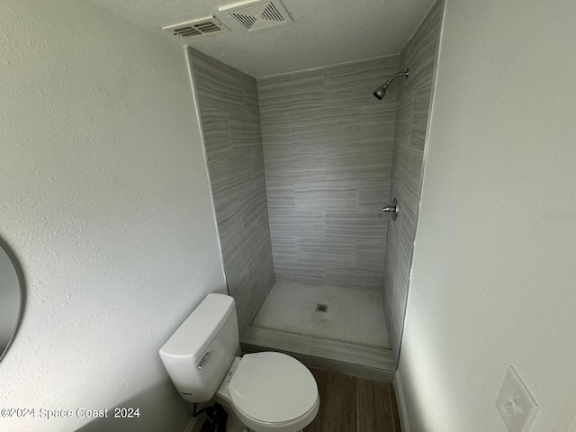 bathroom featuring wood-type flooring, toilet, and tiled shower