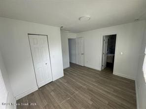 unfurnished bedroom with a closet, ensuite bathroom, and dark wood-type flooring