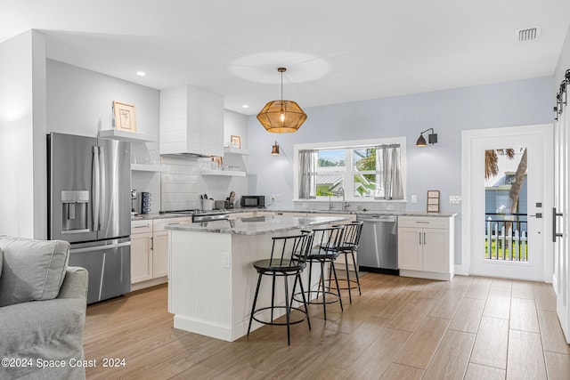 kitchen with light wood-type flooring, white cabinetry, appliances with stainless steel finishes, and decorative light fixtures