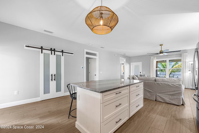 kitchen with light hardwood / wood-style floors, dark stone countertops, white cabinets, a barn door, and a kitchen island