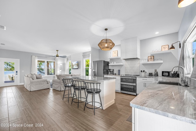 kitchen featuring white cabinets, sink, decorative light fixtures, stainless steel appliances, and a breakfast bar