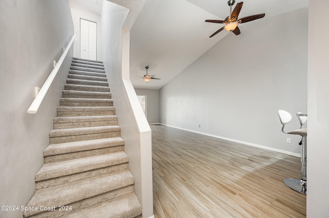 stairs with high vaulted ceiling, ceiling fan, and hardwood / wood-style flooring