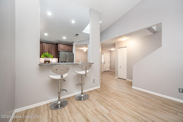 kitchen with stainless steel fridge with ice dispenser, vaulted ceiling, kitchen peninsula, a kitchen breakfast bar, and light hardwood / wood-style flooring