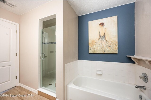 bathroom with a textured ceiling, independent shower and bath, and wood-type flooring