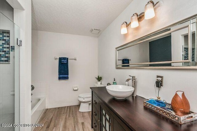 full bathroom featuring wood-type flooring, a textured ceiling, independent shower and bath, vanity, and toilet