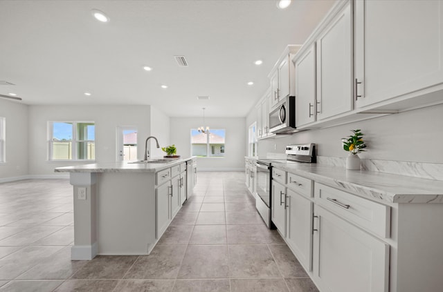 kitchen with light tile patterned flooring, sink, white cabinets, stainless steel appliances, and a center island with sink