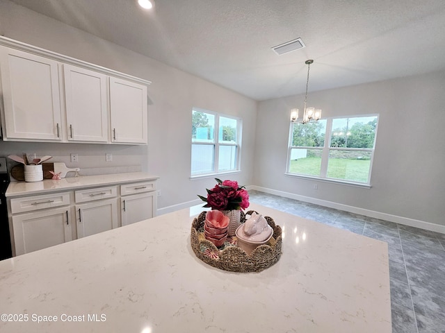 kitchen with white cabinets, baseboards, visible vents, and a chandelier