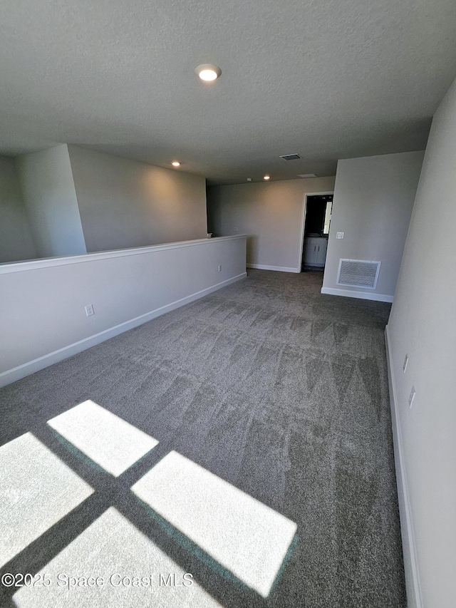 unfurnished room featuring visible vents, a textured ceiling, baseboards, and carpet