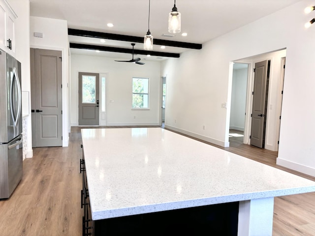 kitchen with beamed ceiling, a kitchen island, light hardwood / wood-style flooring, decorative light fixtures, and stainless steel refrigerator