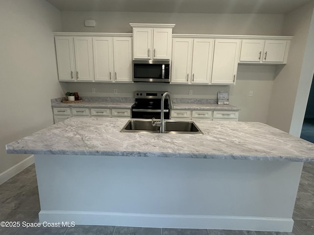 kitchen with a kitchen island with sink, a sink, white cabinetry, appliances with stainless steel finishes, and baseboards