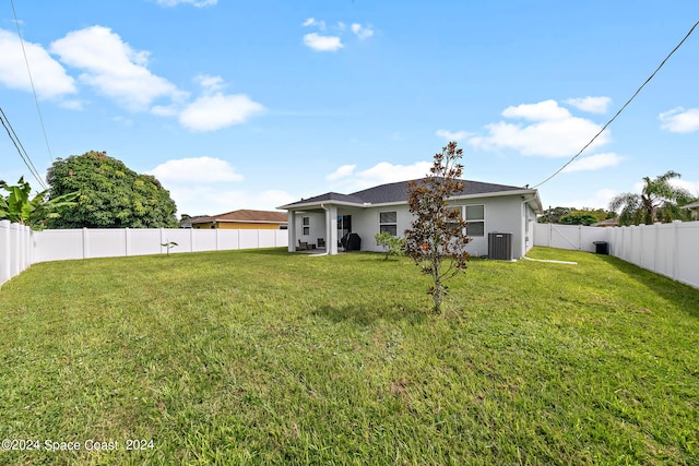 back of house with central AC unit and a yard