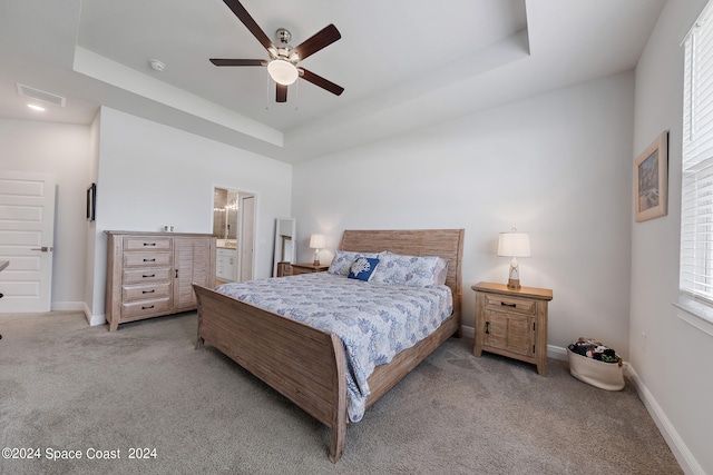 bedroom with ceiling fan, a tray ceiling, ensuite bath, and multiple windows