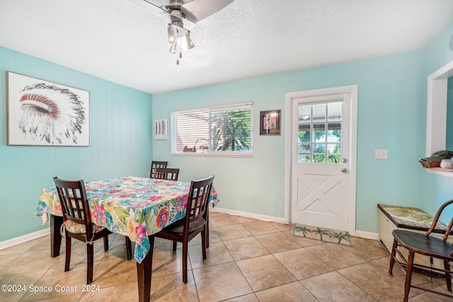 tiled dining space featuring ceiling fan, a textured ceiling, and wooden walls