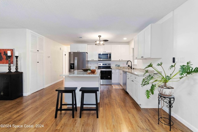 kitchen featuring stainless steel appliances, a center island, white cabinets, hardwood / wood-style flooring, and sink