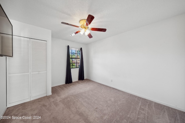 unfurnished bedroom featuring ceiling fan, light colored carpet, a textured ceiling, and a closet