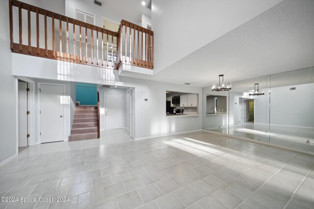 unfurnished living room featuring an inviting chandelier, a towering ceiling, and tile patterned flooring