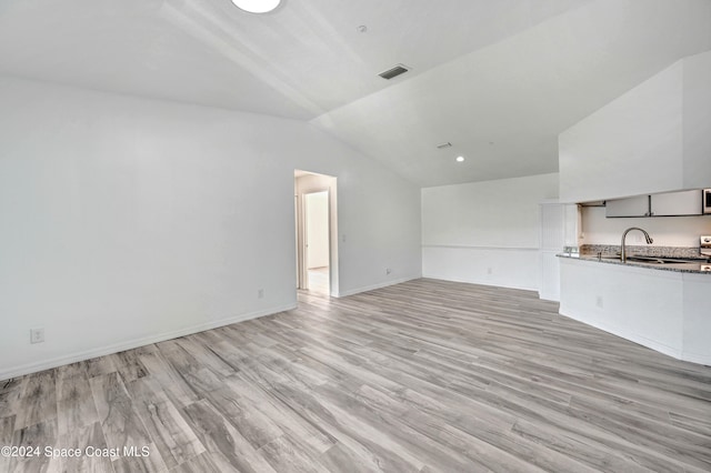 unfurnished living room featuring light hardwood / wood-style floors, sink, and vaulted ceiling