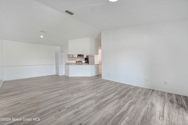 unfurnished living room with lofted ceiling, sink, and light wood-type flooring