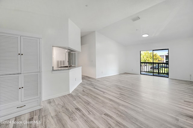 unfurnished living room featuring sink, light hardwood / wood-style floors, and lofted ceiling