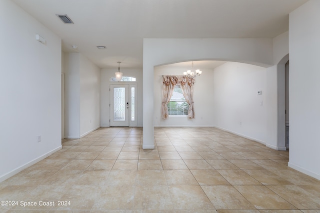 tiled spare room with french doors and a notable chandelier