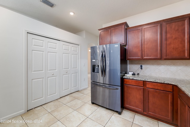 kitchen featuring light stone counters, stainless steel refrigerator with ice dispenser, light tile patterned floors, and decorative backsplash