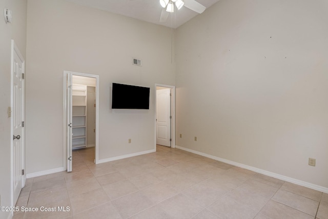 unfurnished bedroom featuring a walk in closet, light tile patterned floors, a closet, and a towering ceiling