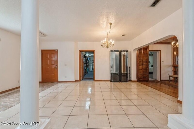 tiled spare room featuring a chandelier, a textured ceiling, and decorative columns