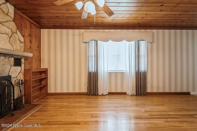 unfurnished living room featuring a stone fireplace, light hardwood / wood-style flooring, wood ceiling, and ceiling fan