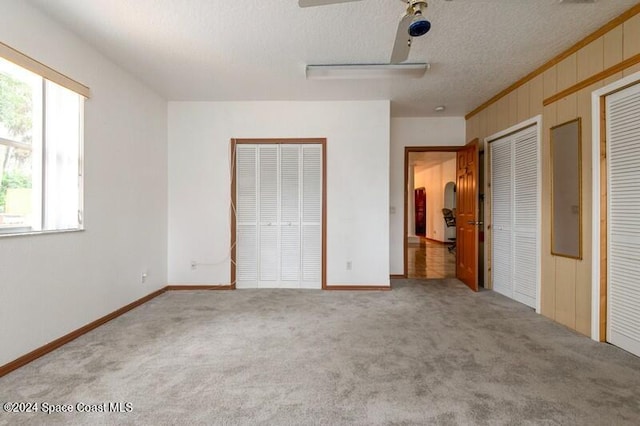 unfurnished bedroom featuring carpet flooring, multiple closets, a textured ceiling, and wooden walls