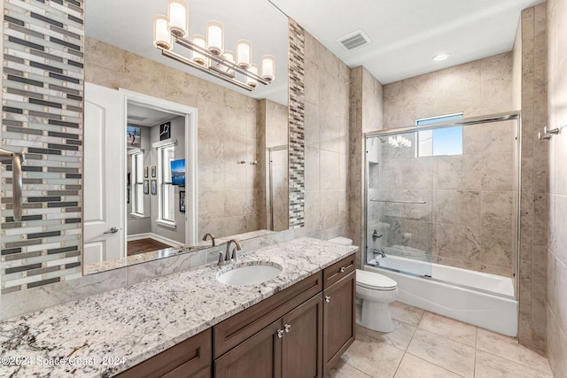 full bathroom with vanity, shower / bath combination with glass door, tile patterned floors, toilet, and tile walls