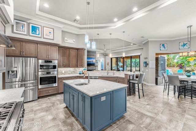 kitchen with light stone countertops, hanging light fixtures, stainless steel appliances, a raised ceiling, and an island with sink