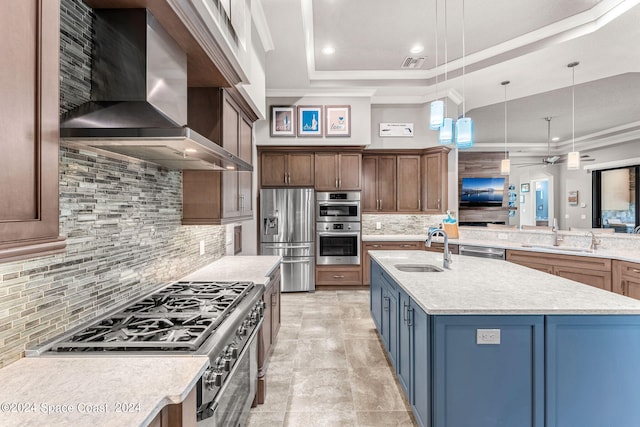 kitchen featuring sink, wall chimney exhaust hood, an island with sink, decorative light fixtures, and stainless steel appliances