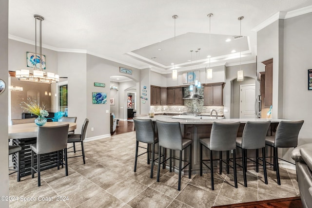 kitchen with tasteful backsplash, wall chimney exhaust hood, dark brown cabinetry, a raised ceiling, and pendant lighting