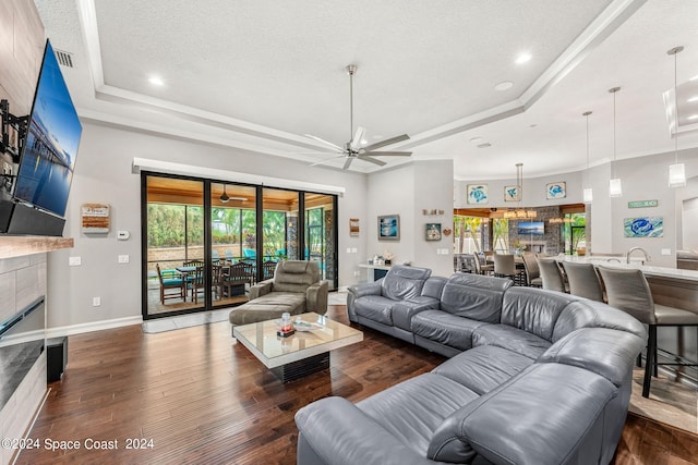 living room with a raised ceiling, ceiling fan, dark hardwood / wood-style floors, ornamental molding, and a textured ceiling