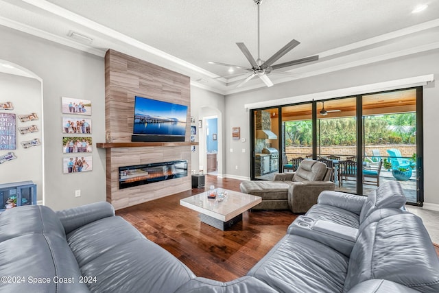 living room with a textured ceiling, ceiling fan, crown molding, a tile fireplace, and hardwood / wood-style flooring