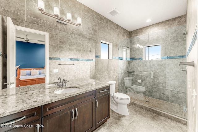 bathroom featuring ceiling fan, toilet, vanity, a shower with shower door, and tile walls