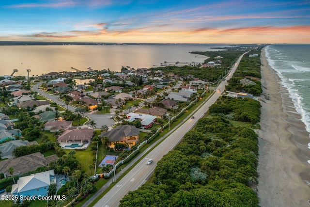 aerial view at dusk featuring a water view and a view of the beach