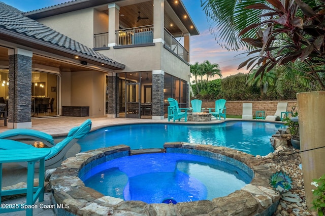 pool at dusk with ceiling fan, an in ground hot tub, and a patio