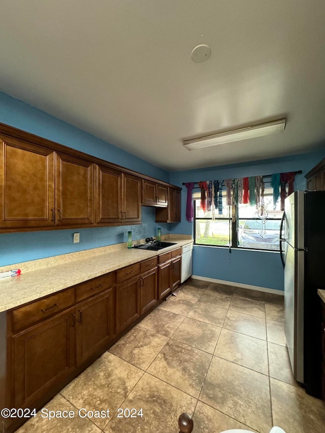 kitchen featuring stainless steel refrigerator, dishwasher, light tile patterned floors, and sink