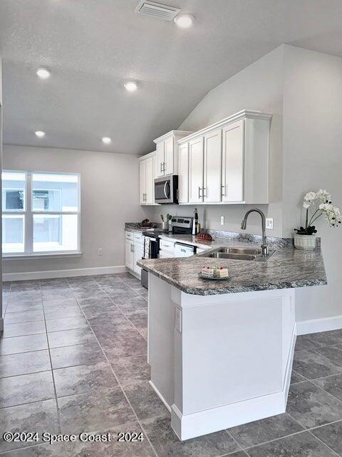1182 Tupelo Cir, Cocoa, FL 32926 - kitchen with stainless steel appliances, a sink, dark stone countertops, vaulted ceiling, and baseboards