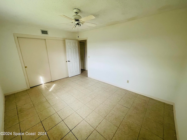 unfurnished bedroom with ceiling fan, a textured ceiling, and a closet