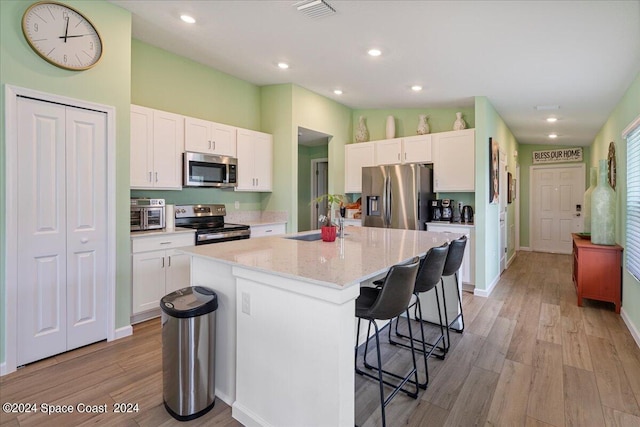 1447 Colebrook Cir SW, Palm Bay, FL 32908 - kitchen with appliances with stainless steel finishes, a sink, a breakfast bar area, white cabinets, and light wood-style floors