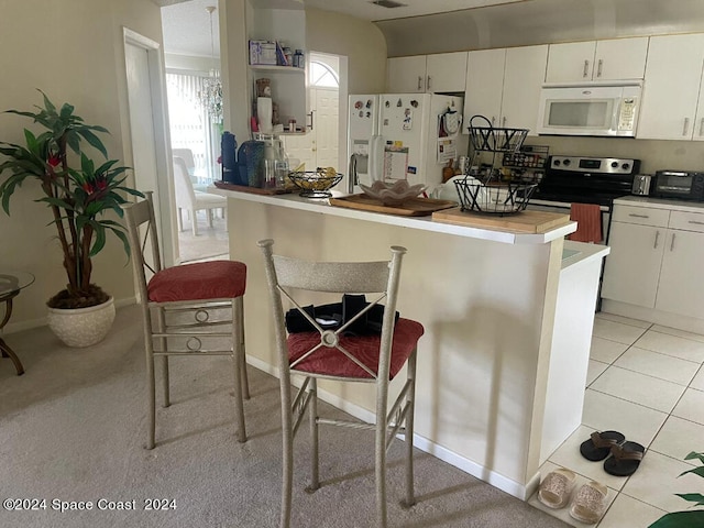 kitchen featuring white cabinets, light tile patterned flooring, a kitchen bar, and white appliances