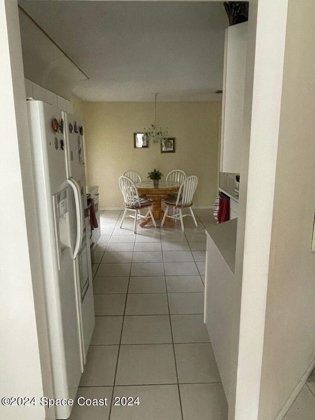 interior space featuring white fridge with ice dispenser, light tile patterned floors, and white cabinetry