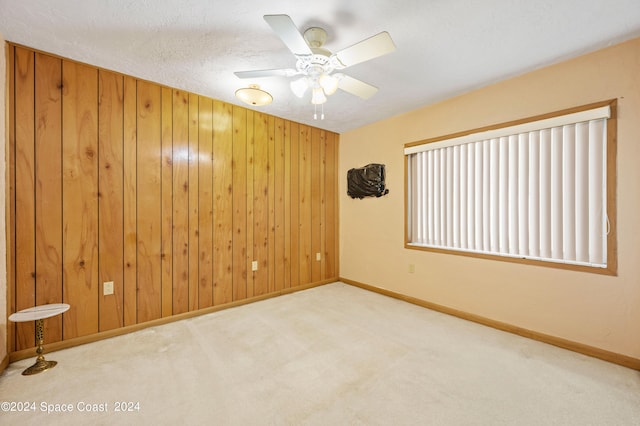 unfurnished room featuring ceiling fan, carpet floors, wooden walls, and a textured ceiling