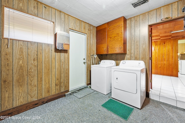 clothes washing area with wooden walls, washer and dryer, light colored carpet, and cabinets