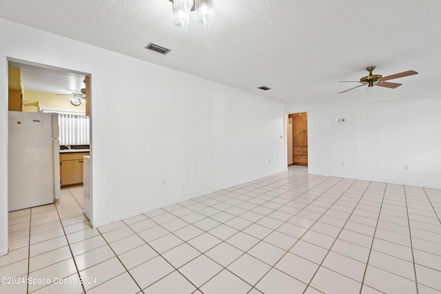 empty room with ceiling fan, light tile patterned flooring, and a textured ceiling